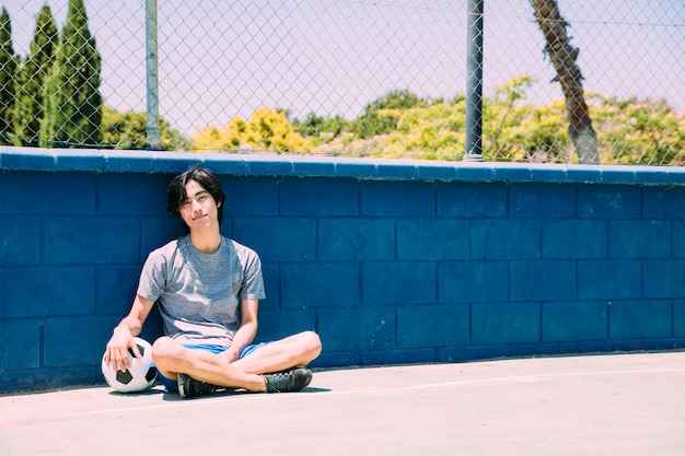 Foto gratuita estudiante adolescente asiático sonriente que se relaja con el balón de fútbol