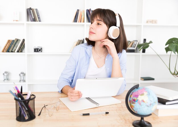 Estudiante adolescente en auriculares blancos sentado a la mesa con tableta