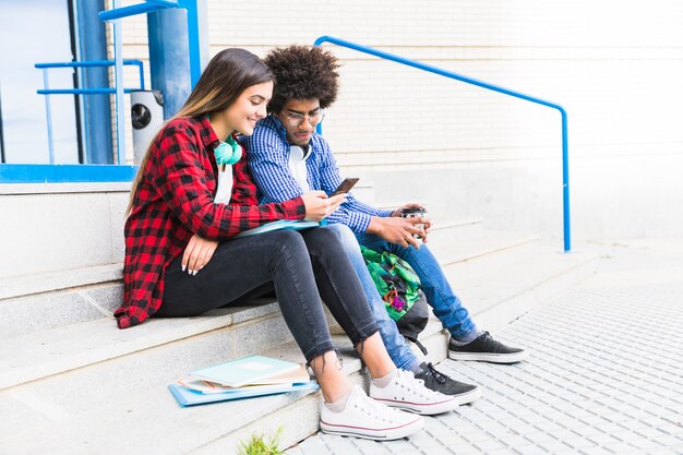 Estudiante adolescente de los pares que se sienta en la escalera blanca usando el teléfono móvil