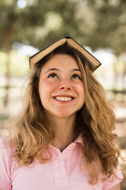 Estudiante adolescente sonriendo con un libro en la cabeza