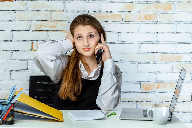 Un estudiante adorable sentado detrás del escritorio y hablando por teléfono Foto de alta calidad