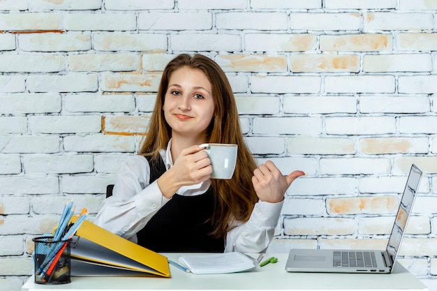 Un estudiante adorable sentado detrás del escritorio sosteniendo una taza de té y sonriendo Foto de alta calidad