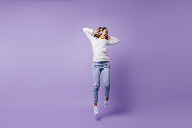 Estudiante afortunada de gran espíritu saltando. Retrato de cuerpo entero de una niña de moda suéter blanco y jeans azul claro.