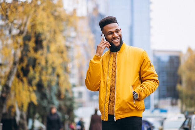 Estudiante afroamericano caminando en la calle y hablando por teléfono