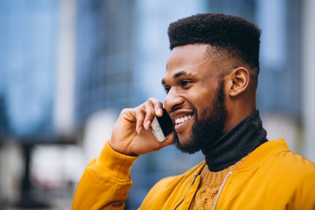 Estudiante afroamericano caminando en la calle y hablando por teléfono