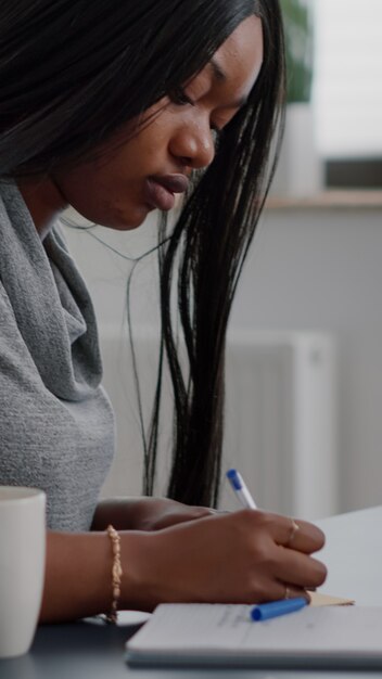 Estudiante afroamericano escribiendo información universitaria en notas stickey poniendo en la computadora
