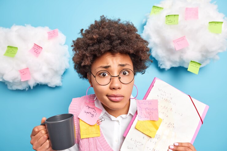 Foto gratuito un estudiante afroamericano rizado desconcertado de la facultad de matemáticas tiene una pausa para el café sostiene una taza con papel para beber con pegatinas de notas hace que la estrategia de los planes del proyecto se prepara para los exámenes usa anteojos transparentes redondos