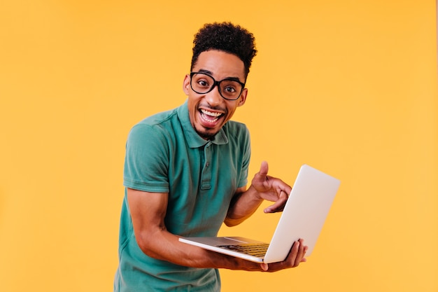 Estudiante alegre en camiseta verde posando con portátil. Foto interior del autónomo masculino asombrado aislado.