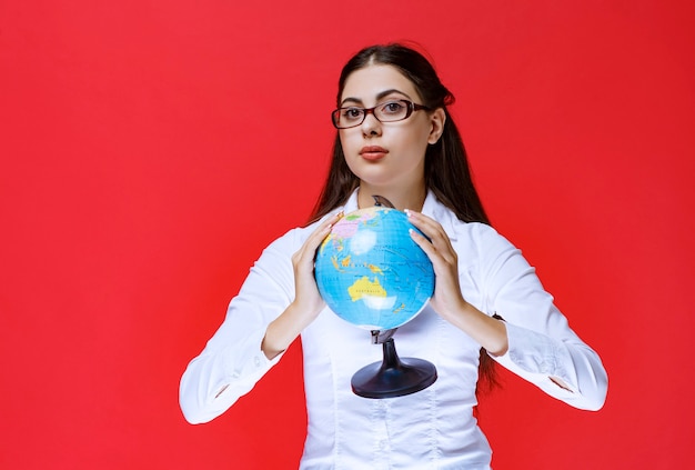 Foto gratuita estudiante en anteojos sosteniendo e introduciendo un globo terráqueo.