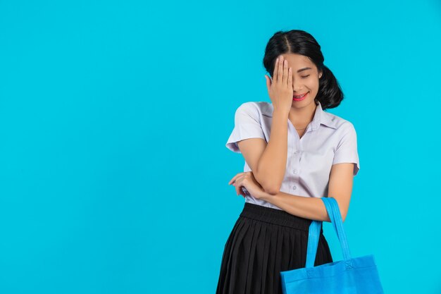 Una estudiante asiática que hace girar una bolsa de tela y muestra varios gestos en un azul.