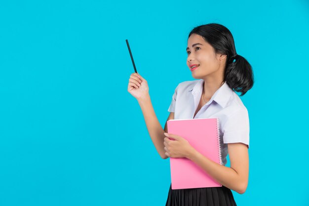 Una estudiante asiática con una con su cuaderno rosa sobre un azul.