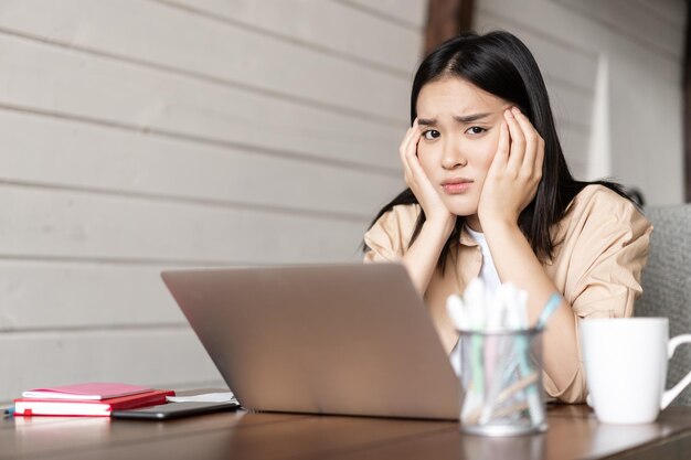 Estudiante asiática triste sentada aburrida con la computadora portátil en casa cansada o aburrida de estudiar ...