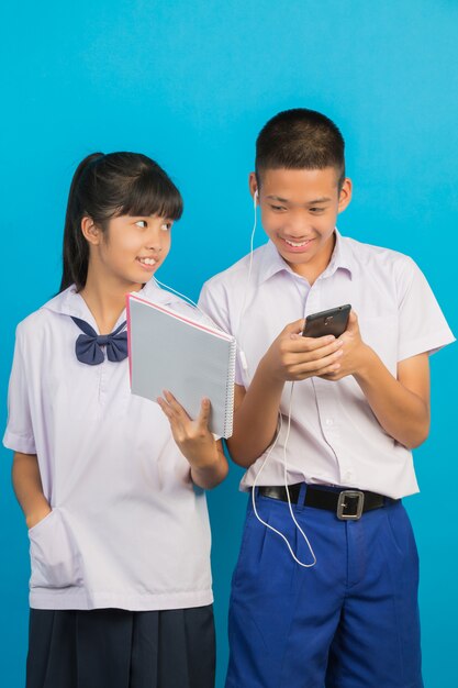 Un estudiante asiático que sostiene un cuaderno y un estudiante masculino asiático que se coloca que juega en el azul.