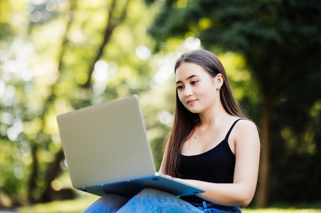 Estudiante asiático que trabaja con la computadora portátil al aire libre campus universitario green park concept