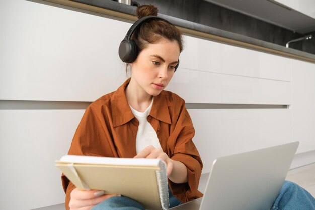 Foto gratuita una estudiante de aspecto serio que estudia en casa se sienta con una computadora portátil y un cuaderno en el suelo haciendo la tarea