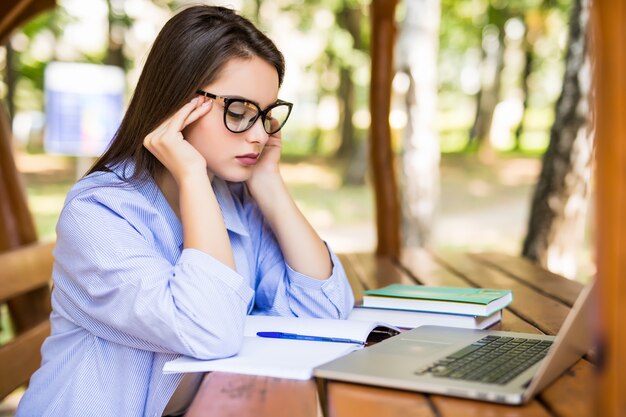 Foto gratuita estudiante cansado usando una computadora portátil en una mesa del parque al final del día