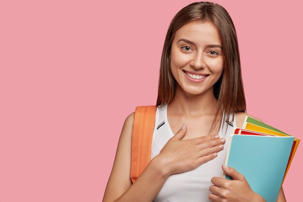 Estudiante complacido amistoso posando contra la pared rosa