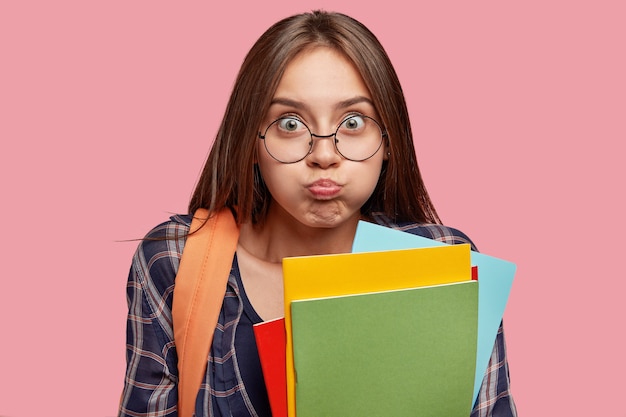 Estudiante divertido posando contra la pared rosa con gafas