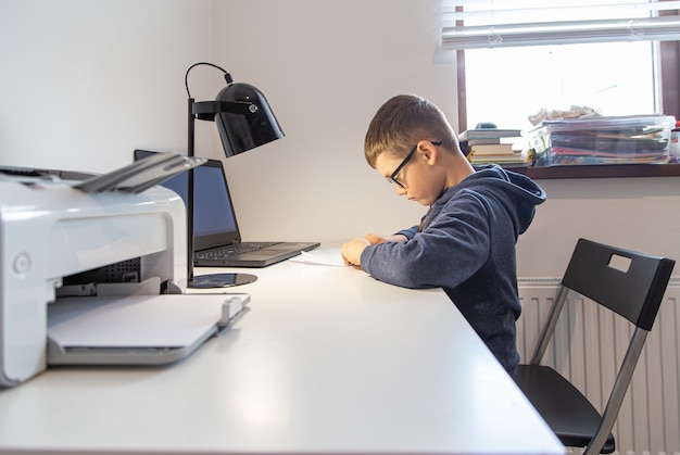 Un estudiante de escuela primaria aprende de forma remota en casa frente a una computadora portátil en su escritorio.