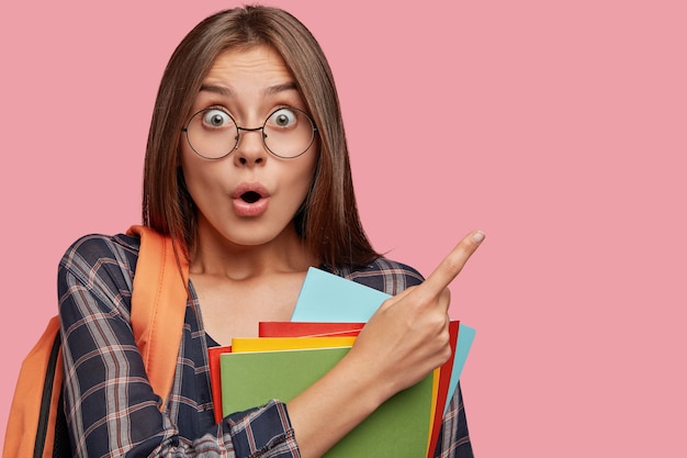 Estudiante estupefacto posando contra la pared rosa con gafas