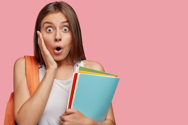 estudiante estupefacto posando contra la pared rosa