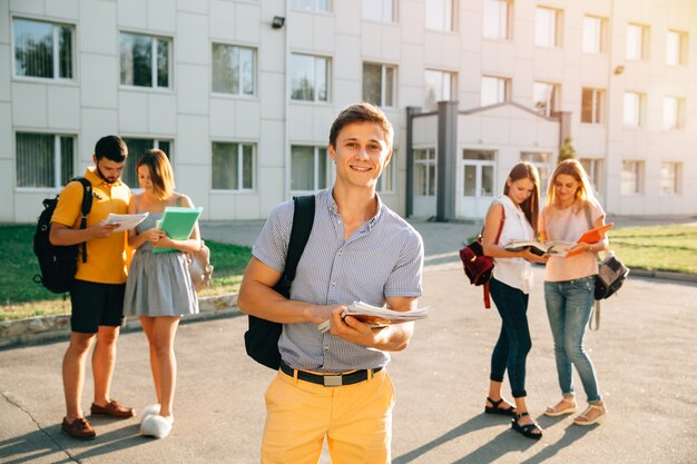 Estudiante feliz con cuadernos y mochila sonriendo mientras está de pie