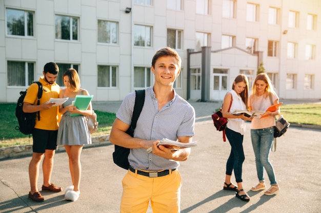 Estudiante feliz con cuadernos y mochila sonriendo mientras está de pie