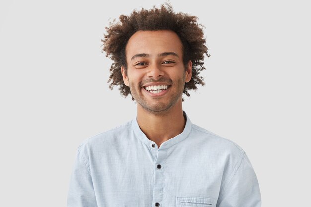Estudiante feliz con peinado afro muestra dientes blancos, estando de buen humor después de clases
