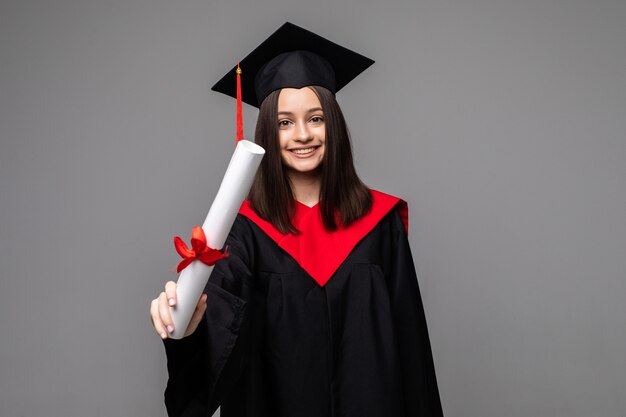 Estudiante feliz con sombrero de graduación y diploma en gris