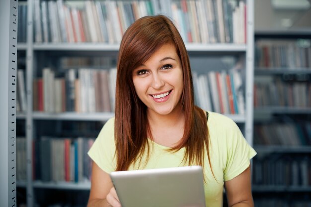 Estudiante feliz usando tableta digital en biblioteca