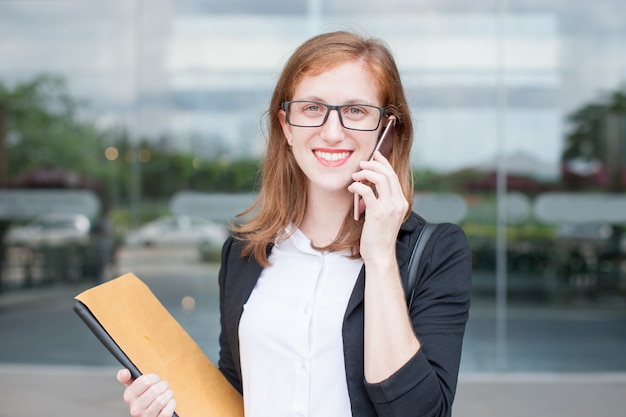 Estudiante femenina feliz que llama en el teléfono al aire libre