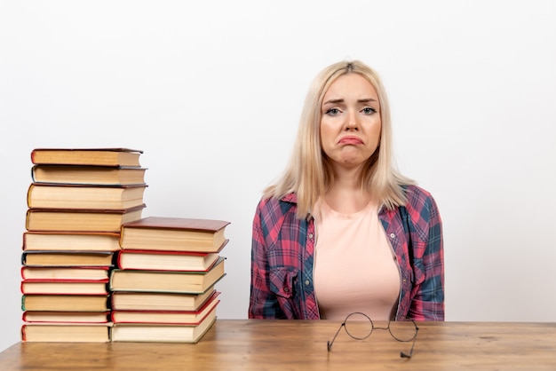 estudiante femenina sentada con libros con expresión triste en blanco