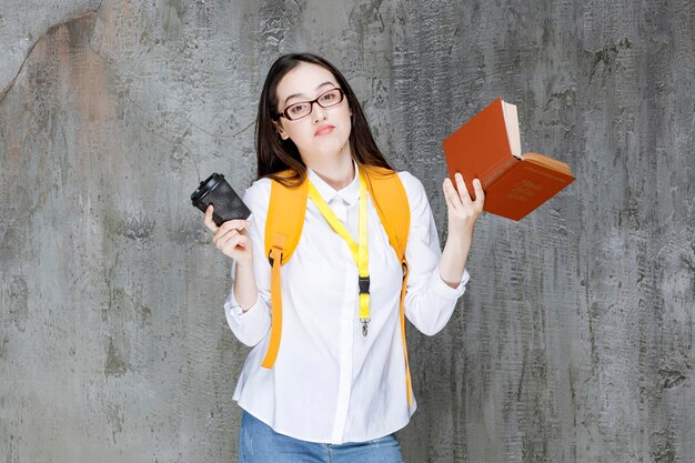 Estudiante con gafas sosteniendo un libro y una taza de café. foto de alta calidad