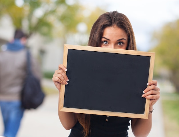 Estudiante graciosa cubriendo su cara con una pizarra