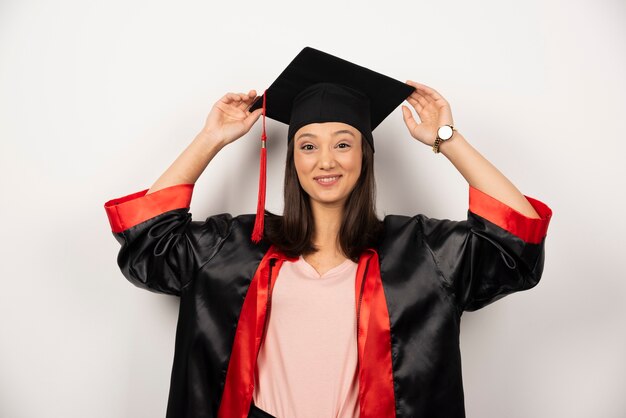 Estudiante graduado feliz en vestido posando sobre fondo blanco.