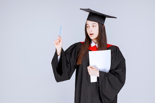 Estudiante graduado con papel y bolígrafo de pie antes de que comience la ceremonia. Foto de alta calidad