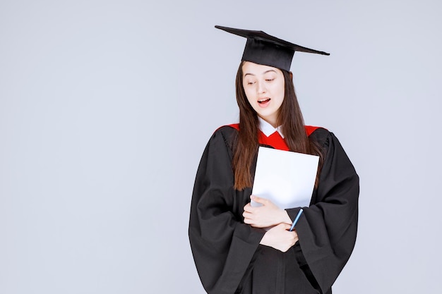 Estudiante graduado con papel y bolígrafo de pie antes de que comience la ceremonia. Foto de alta calidad