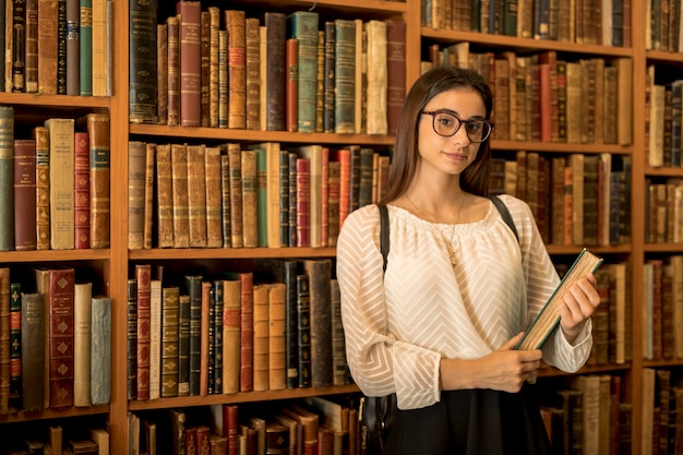 Estudiante inteligente con el libro en la biblioteca