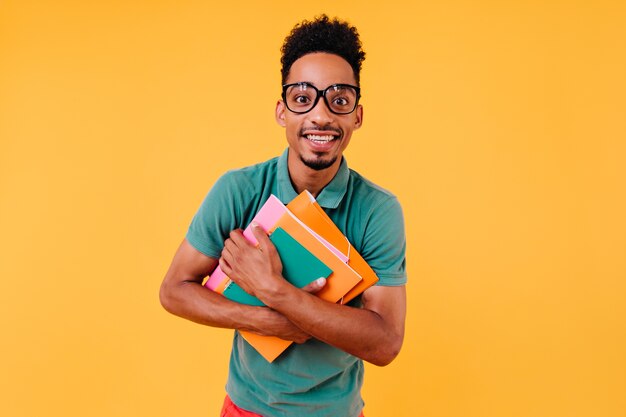 Estudiante internacional alegre posando después de las lecciones. Chico inteligente interesado en vasos con libros.