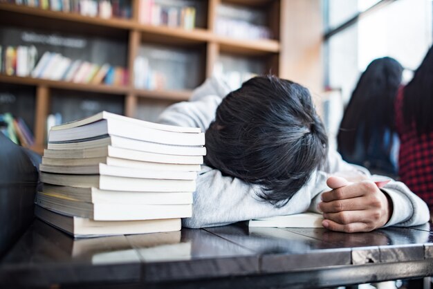 El estudiante joven barbudo durmiente miente en las manos en café