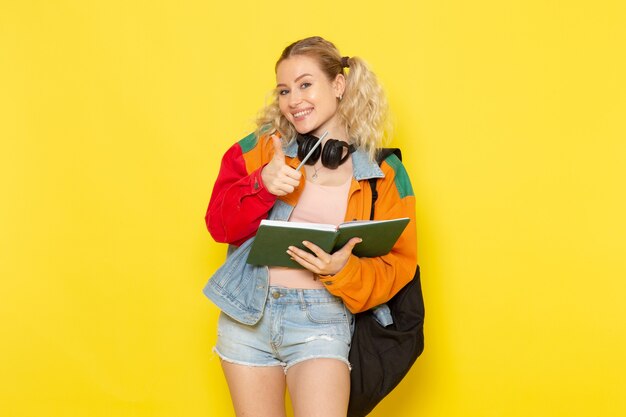 Estudiante joven en ropa moderna sonriendo sosteniendo cuadernos en amarillo