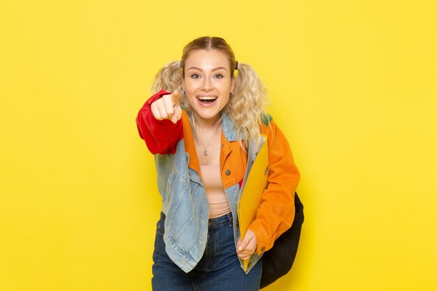 Estudiante joven en ropa moderna sosteniendo archivos amarillos riendo sobre amarillo