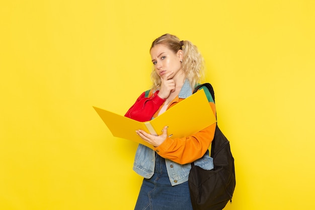 Estudiante joven en ropa moderna sosteniendo archivos pensando en amarillo