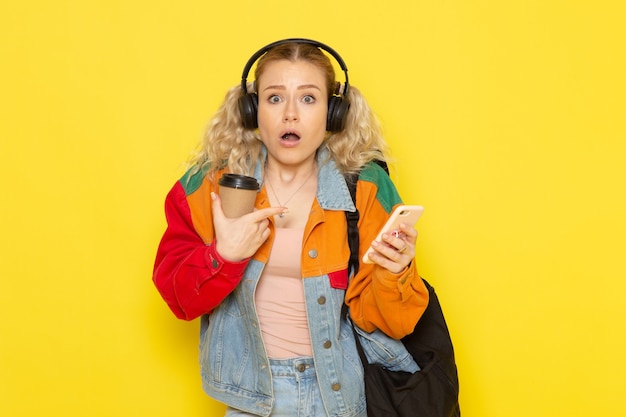 Estudiante joven en ropa moderna sosteniendo café lsitening a la música en amarillo