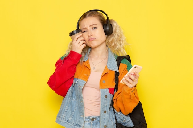 Estudiante joven en ropa moderna sosteniendo café y teléfono en amarillo