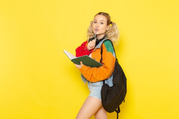 Estudiante joven en ropa moderna sosteniendo cuaderno en amarillo