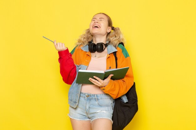 Estudiante joven en ropa moderna sosteniendo cuaderno riendo sobre amarillo