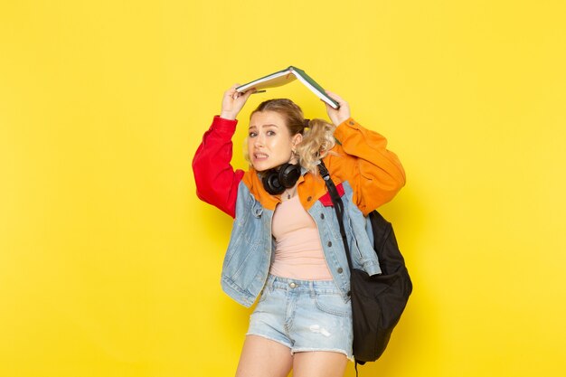 Estudiante joven en ropa moderna sosteniendo cuadernos en amarillo