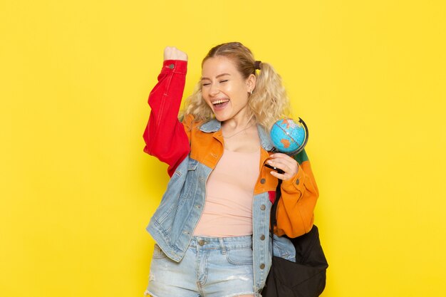 Estudiante joven en ropa moderna sosteniendo globo con cara feliz en amarillo