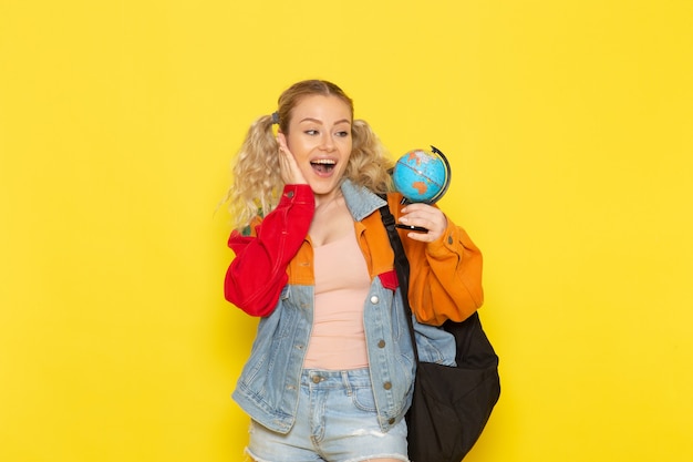 Estudiante joven en ropa moderna sosteniendo pequeño globo con sonrisa en amarillo